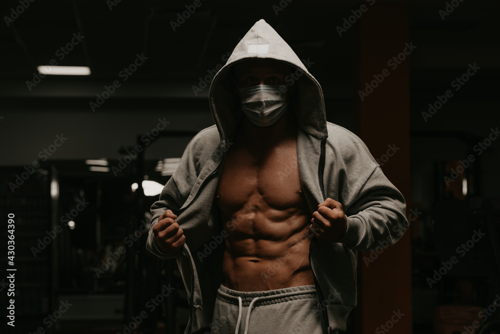 A bodybuilder in the hood and a face mask to avoid the spread of  coronavirus is