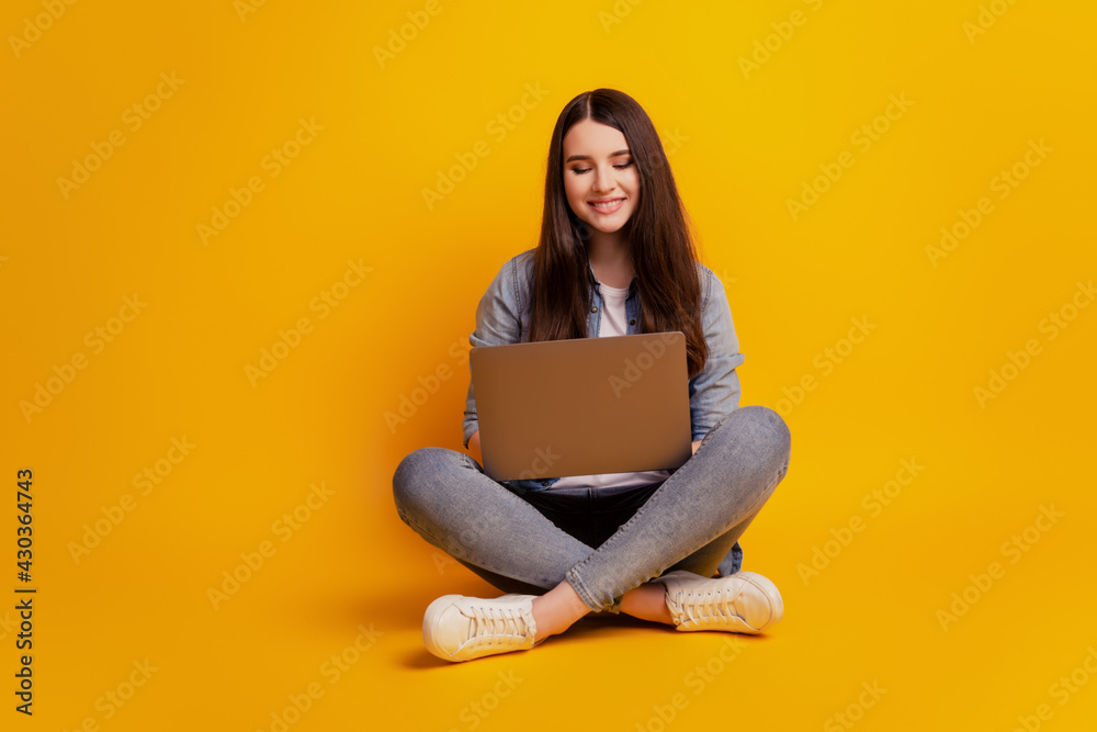 Naklejka premium Portrait of girl with laptop sit floor crossed legs on yellow background