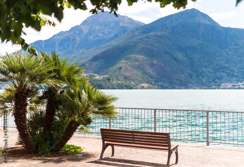 Scene with no people palm and empty bench in front of the lake and mountain in Como Italy