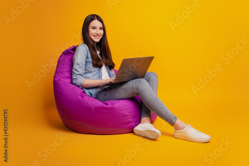 Portrait of girl with laptop sit beanbag look camera on yellow background