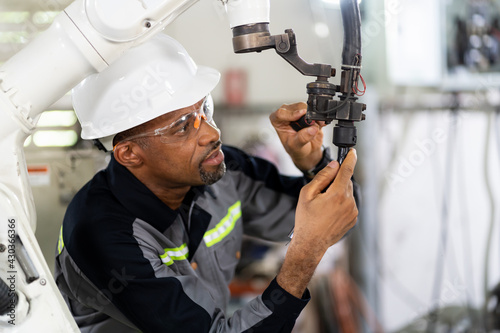 African American male engineer worker maintenance automatic robotic arm machine in factory. Black male technician worker checking, repair automatic robot hand machine with screwdriver in smart factory