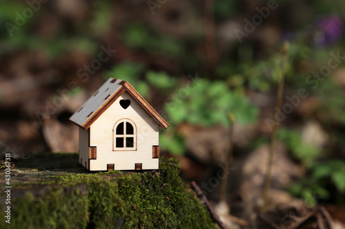 Wooden house model in a forest on mossy stump on spring flowers background. Concept of country cottage, real estate in ecologically clean area, vivid colors of fairy nature