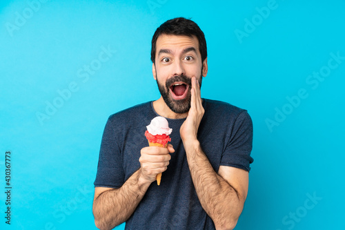 Young man with a cornet ice cream over isolated blue background with surprise and shocked facial expression