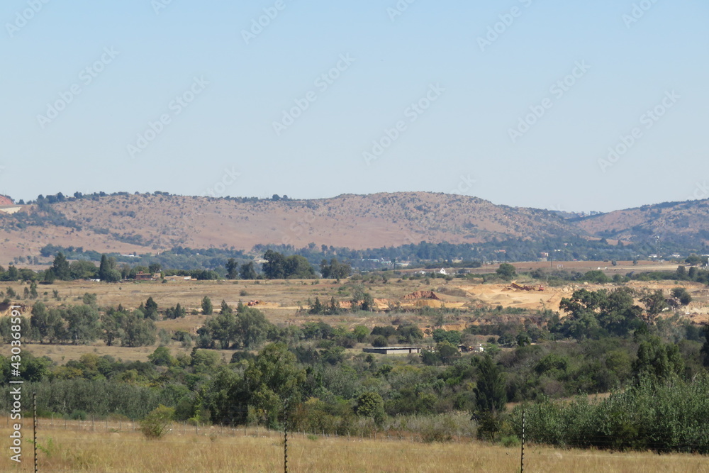 A scenic autumn colored landscape photograph of grasslands and bushes and scattered trees with hilltops on the horizon under a blue sky