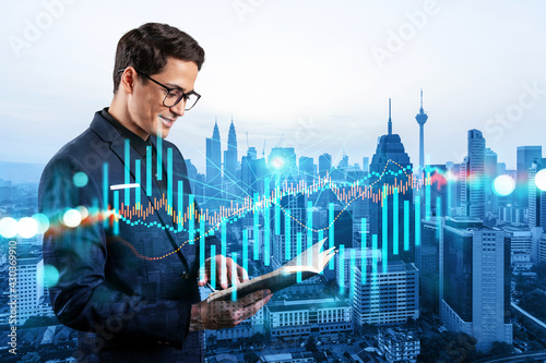 A young eastern handsome trader in suit examine his notes to predict the market behavior based on historic data and stock market. Corporate finance fund and forex chart. Kuala Lumpur. Double exposure