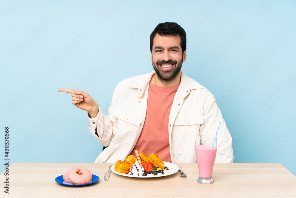 Man at a table having breakfast waffles and a milkshake pointing finger to the side Man at a table having breakfast waffles and a milkshake pointing finger to the side