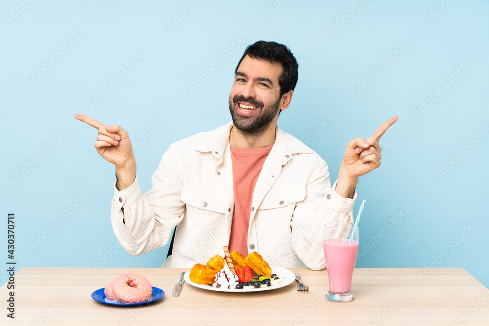 Man at a table having breakfast waffles and a milkshake pointing finger to the laterals and happy Man at a table having breakfast waffles and a milkshake pointing finger to the laterals and happy