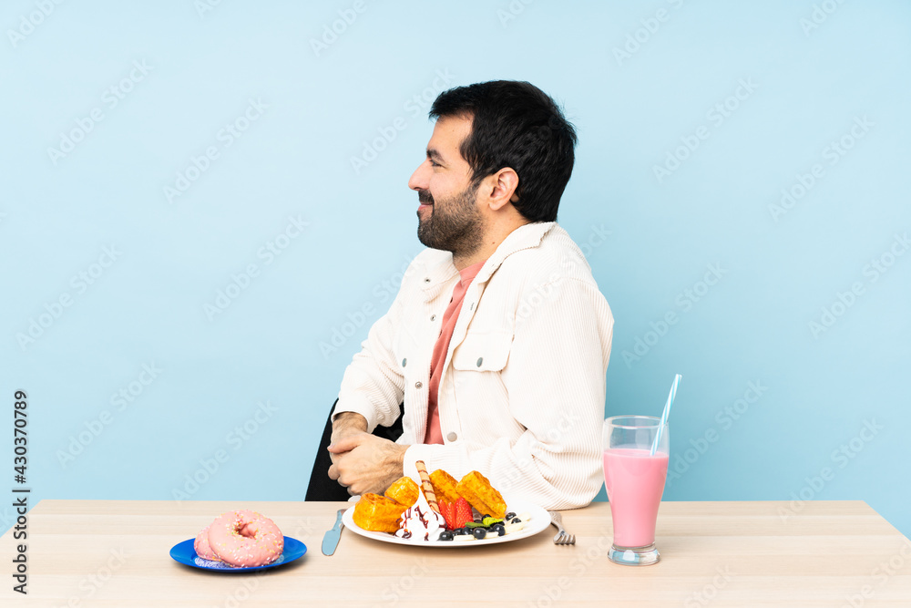 Man at a table having breakfast waffles and a milkshake in lateral position Man at a table having breakfast waffles and a milkshake in lateral position