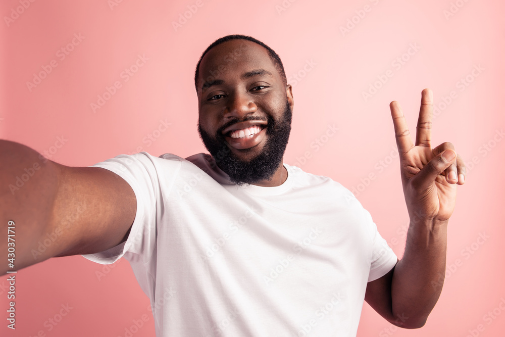 Portrait of cheerful positive man take selfie show v-sign beaming smile on pink wall Portrait of cheerful positive man take selfie show v-sign beaming smile on pink wall
