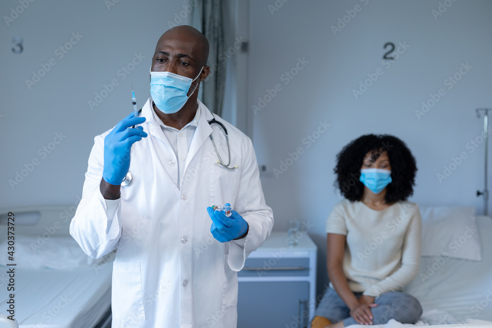 Naklejka premium African american male doctor in face mask and gloves preparing covid vaccination for sick patient