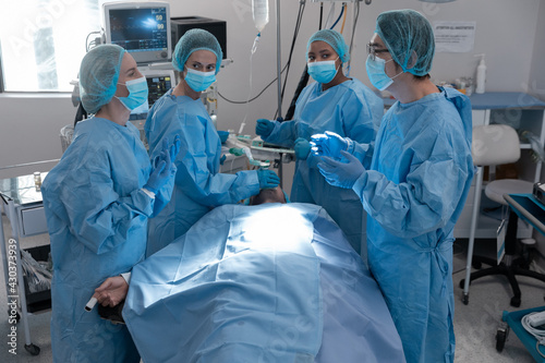 Diverse group of male and female surgeons in operating theatre wearing face masks performing surgery