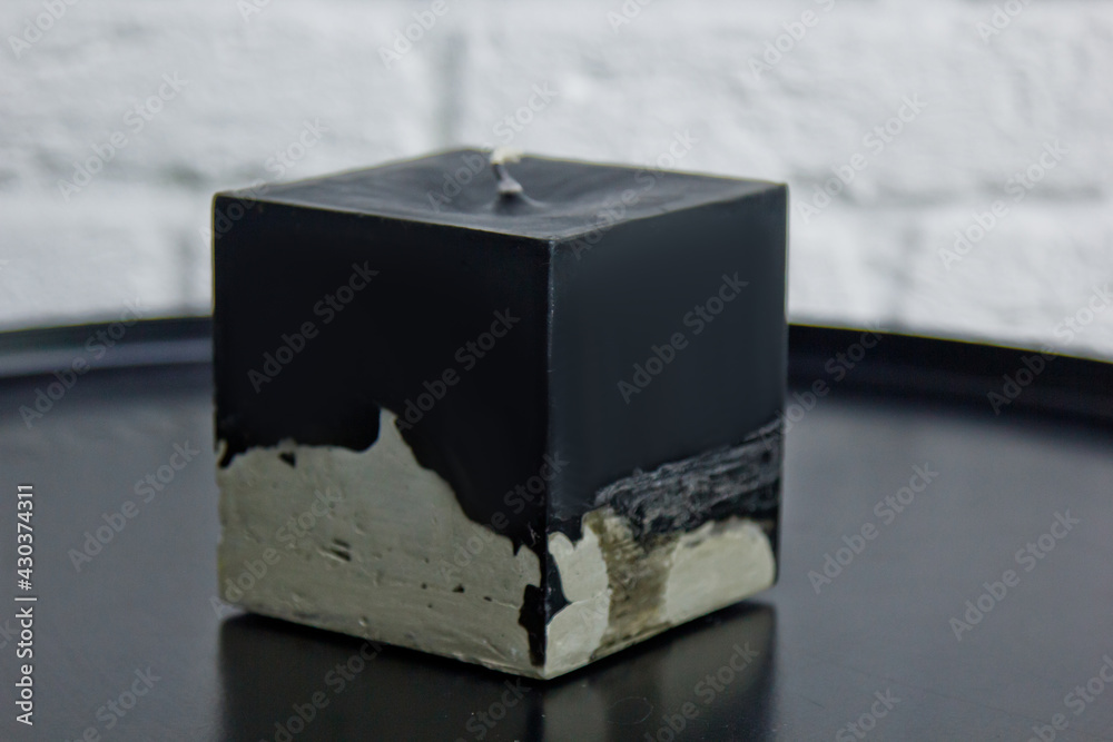 homemade black candle with concrete on the background of a white wall. handmade decor close-up. Details of colored candle in loft style in the shape of a cube