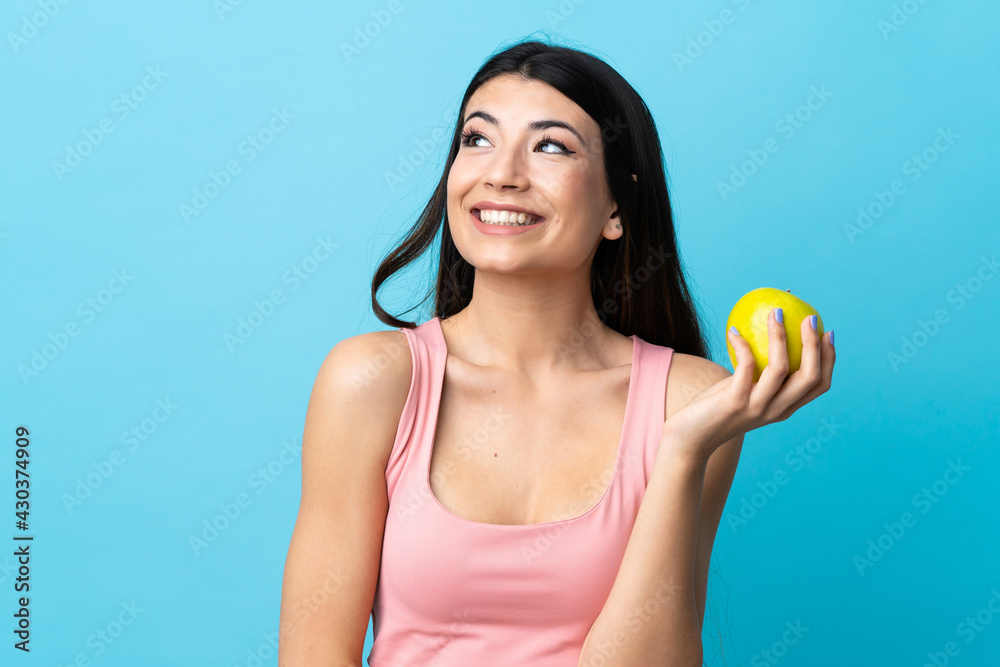 Young brunette girl over isolated blue background with an apple and happy Young brunette girl over isolated blue background with an apple and happy
