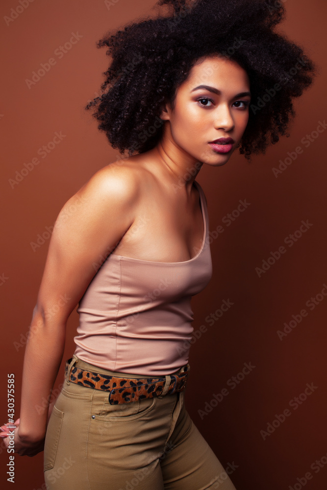Naklejka premium pretty young african american woman with curly hair posing cheerful gesturing on brown background, lifestyle people concept