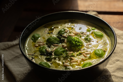 Broccoli cream soup decorating with seeds, basil, olive oil in a black bowl on a wooden table