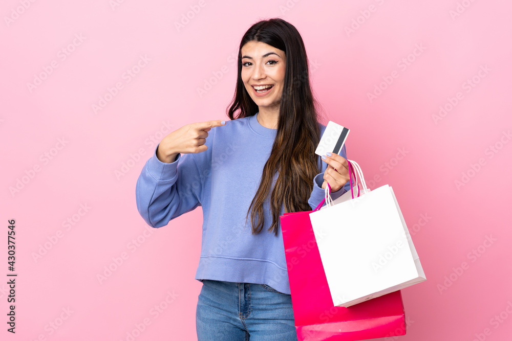 Young brunette girl over isolated pink background holding shopping bags and a credit card Young brunette girl over isolated pink background holding shopping bags and a credit card