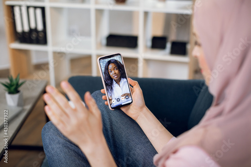 Billede på lærred View from the shoulder of phone screen with pleasant black woman doctor, consulting patient online