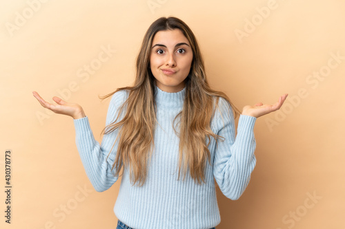 Young caucasian woman isolated on beige background making doubts gesture