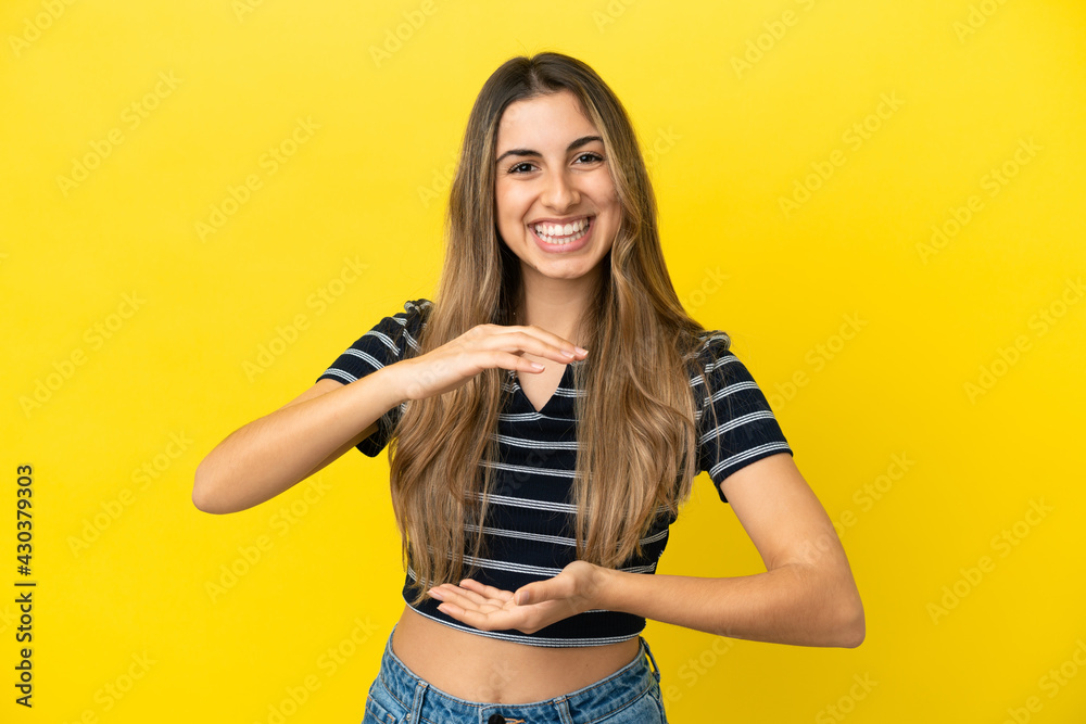 Young caucasian woman isolated on yellow background holding copyspace imaginary on the palm to insert an ad Young caucasian woman isolated on yellow background holding copyspace imaginary on the palm to insert an ad