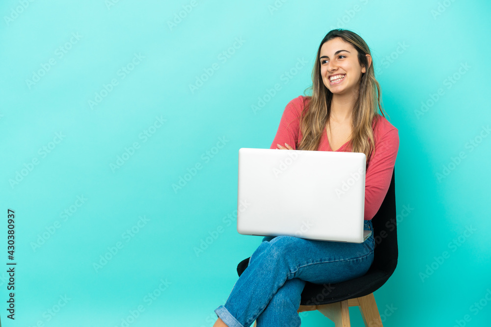 Young caucasian woman sitting on a chair with her pc isolated on blue background happy and smiling Young caucasian woman sitting on a chair with her pc isolated on blue background happy and smiling