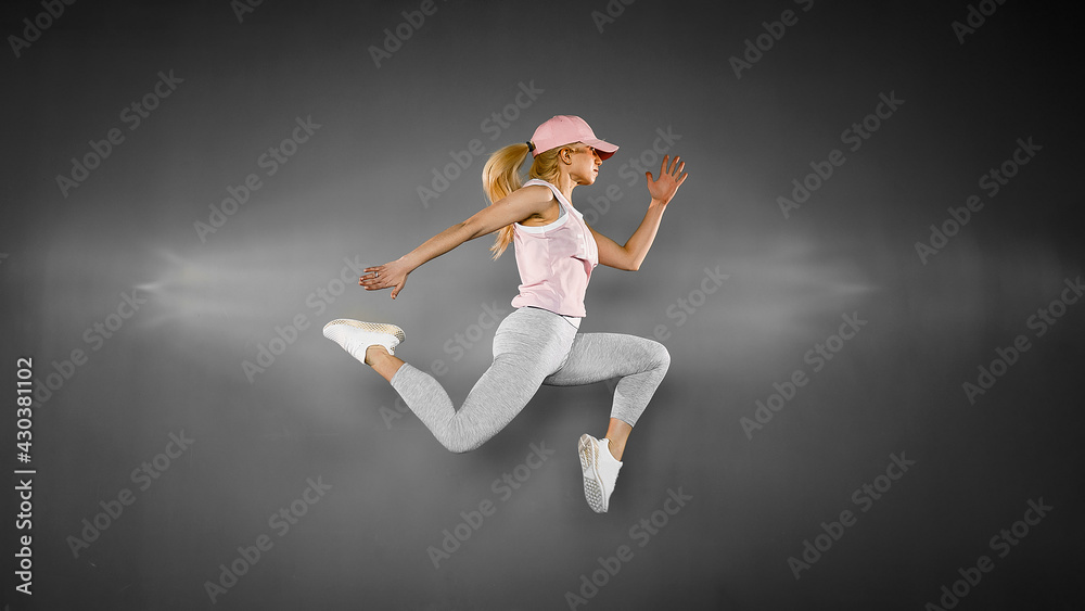 Young woman with fit body jumping and running against grey backg