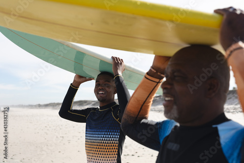 African american father and son carrying surfboards on their heads at the beach photo