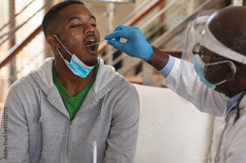 African american senior male doctor performing throat swab test on african american man at home photo