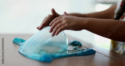 Little girl playing with slimy plasticine creating a bubble with blue slime