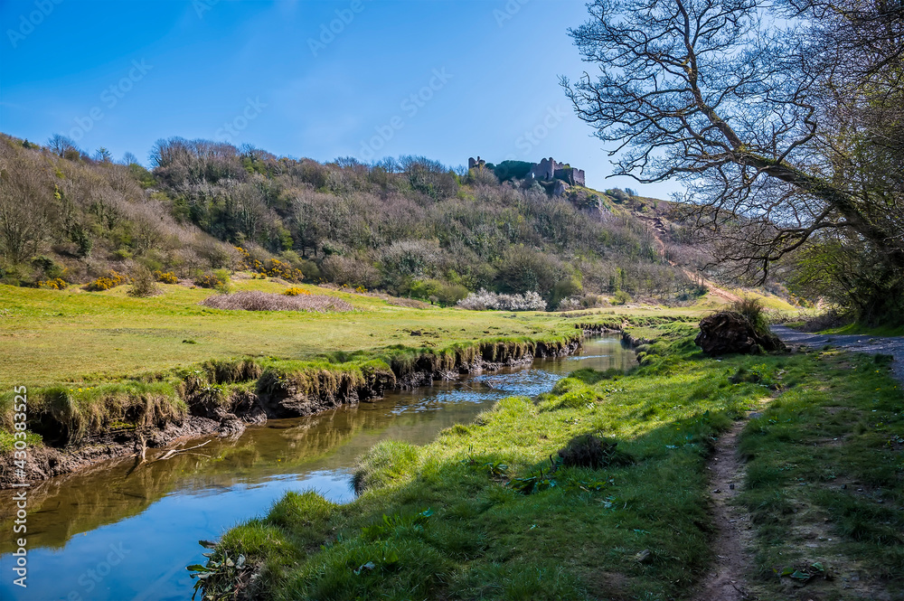 A view along the Pennard Pill stream floodplain towards the castle ruins at the Three Cliffs Bay, Gower Peninsula, Swansea, South Wales on a sunny day A view along the Pennard Pill stream floodplain towards the castle ruins at the Three Cliffs Bay, Gower Peninsula, Swansea, South Wales on a sunny day