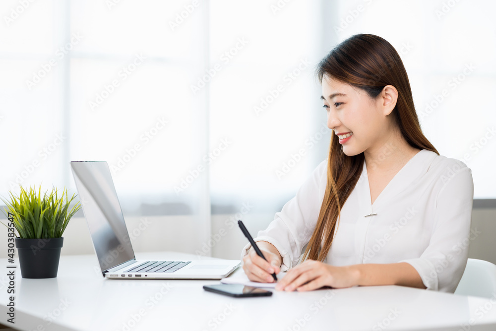 Young asian beautiful business woman working with laptop sitting at home and note on book. Smiling charming happy young female doing homework meeting conference with team at home. Young asian beautiful business woman working with laptop sitting at home and note on book. Smiling charming happy young female doing homework meeting conference with team at home.
