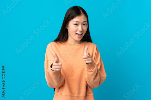 Young Chinese girl over isolated blue background pointing to the front and smiling