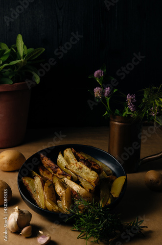 Potato wedges on dark background, cooking process. Process of making a rustic recipe of aromatic baked potatoes. food styling