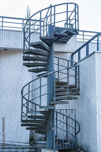 Winding spiral staircase outdoors. Steel or metal curved stairs. Outside circular  stairway with top of the building and bright sky