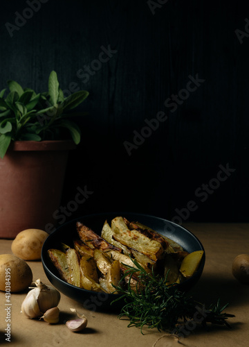 Potato wedges on dark background, cooking process. Process of making a rustic recipe of aromatic baked potatoes. food styling