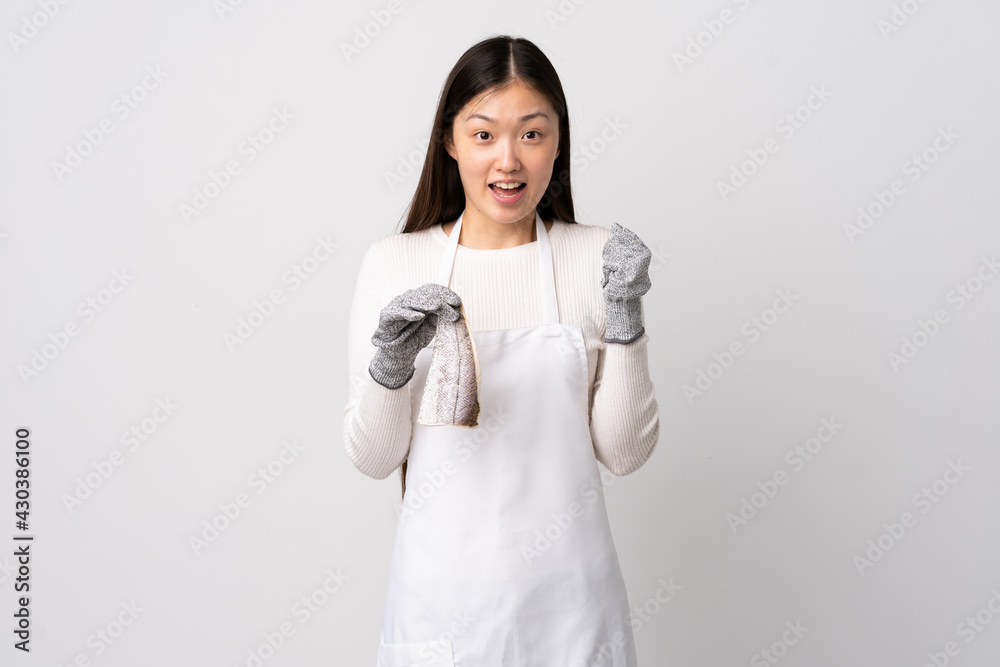 Chinese fishmonger wearing an apron and holding a raw fish over isolated white background celebrating a victory in winner position Chinese fishmonger wearing an apron and holding a raw fish over isolated white background celebrating a victory in winner position