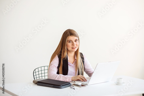 Business woman is working on her laptop in her office. White wall background. Woman at work, employee, office worker. 