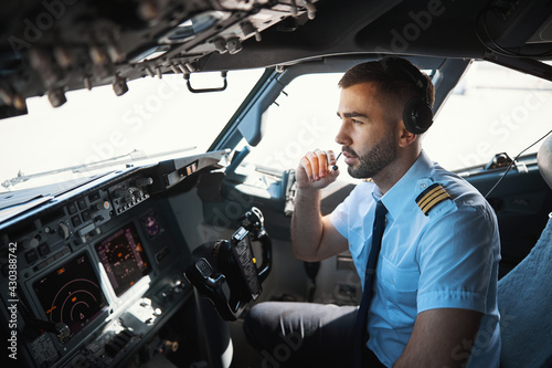 Serious pilot talking to the coworkers in the microphone