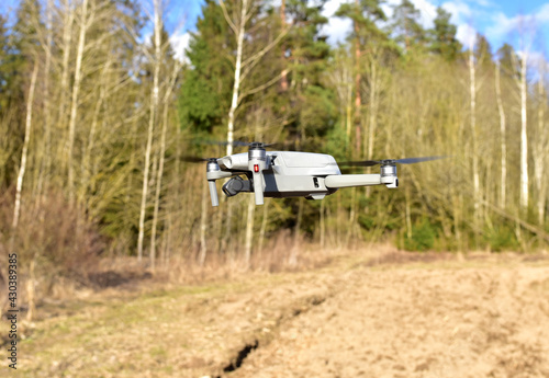 Drone in flight against the background of a forest and a field during observation