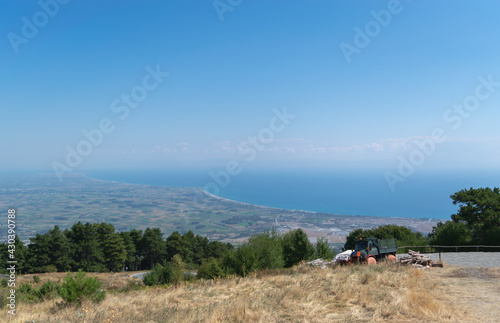 View from the mountain to the valley and the blue sea. A lonely truck is standing on a hill, and just below is an asphalt highway. Blue sky with white cumulus clouds. Summer time. Horizontal photo. 