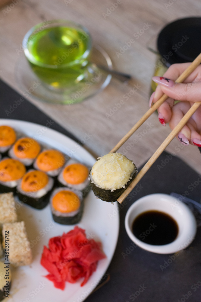 Woman holding sushi with chopsticks over plate of sushi Woman holding sushi with chopsticks over plate of sushi