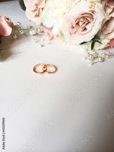 Pink flowers, pearl jewelry and two gold wedding rings on a white background. Wedding concept. Isolated	