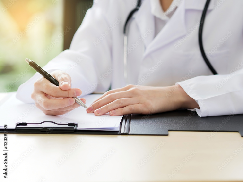 A close-up of the hand of a female doctor or nurse is using a pen writing information or something with a blurred background. A close-up of the hand of a female doctor or nurse is using a pen writing information or something with a blurred background.