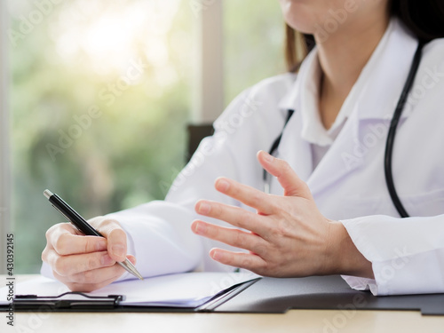 A close-up of the hand of a female doctor or nurse is holding a pen and using another hand to explain information or something with a blurred background.