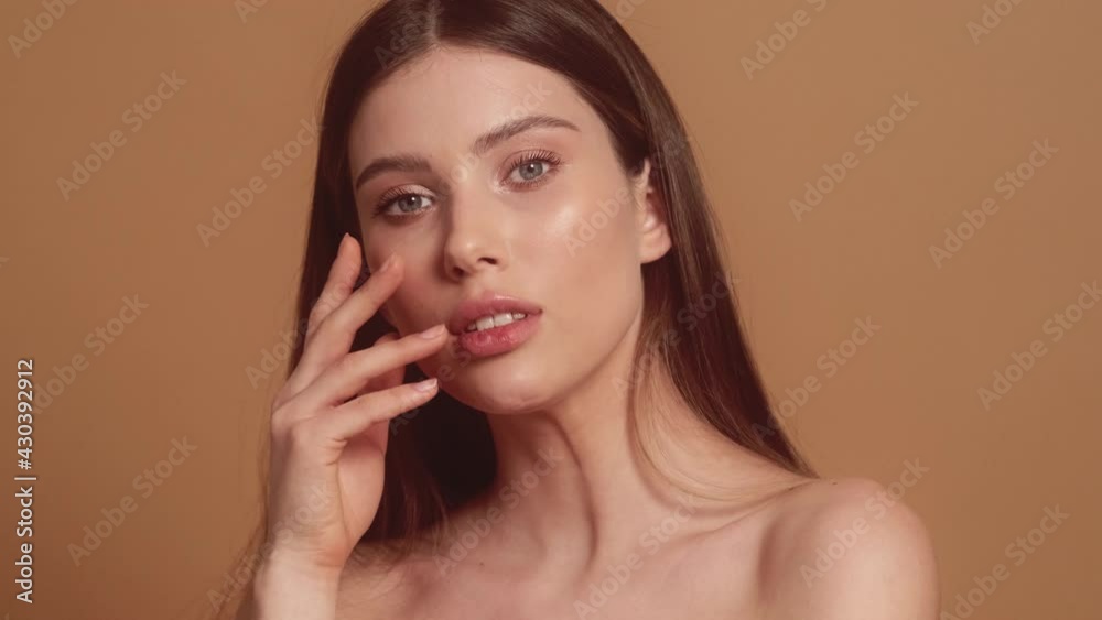 A gorgeous young half-naked woman is posing to the camera standing isolated over a beige background in the studio A gorgeous young half-naked woman is posing to the camera standing isolated over a beige background in the studio