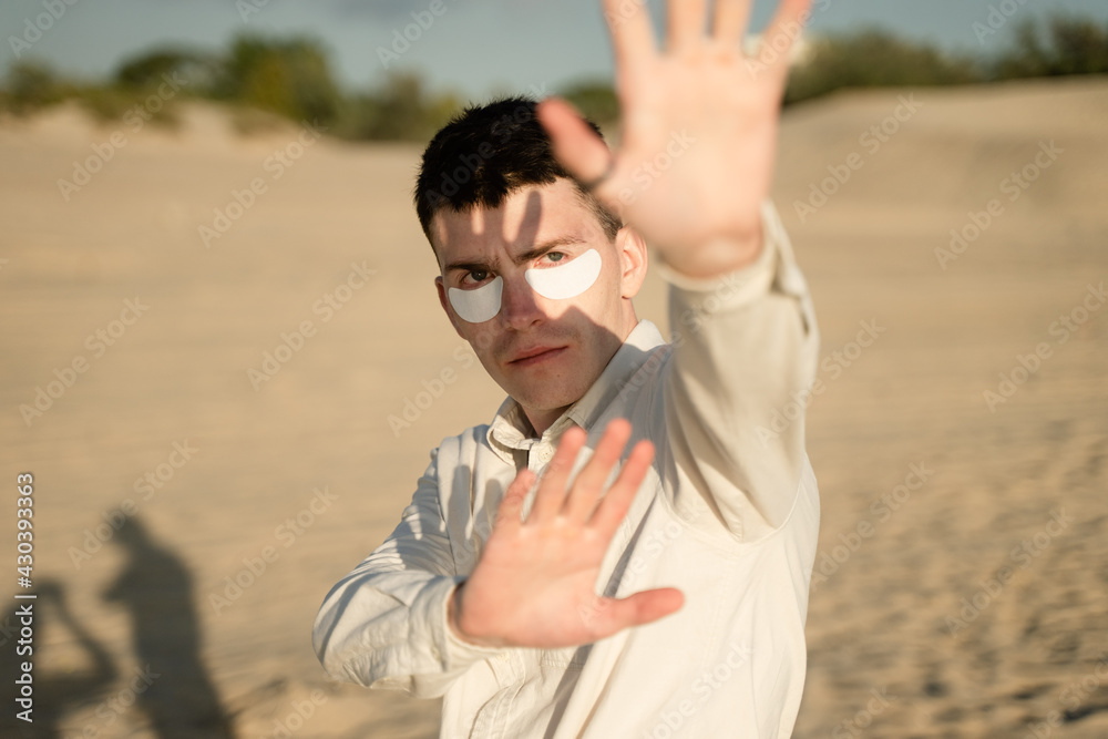 young guy wearing white patches under his eyes protects himself from the sun's rays with his hands young guy wearing white patches under his eyes protects himself from the sun's rays with his hands