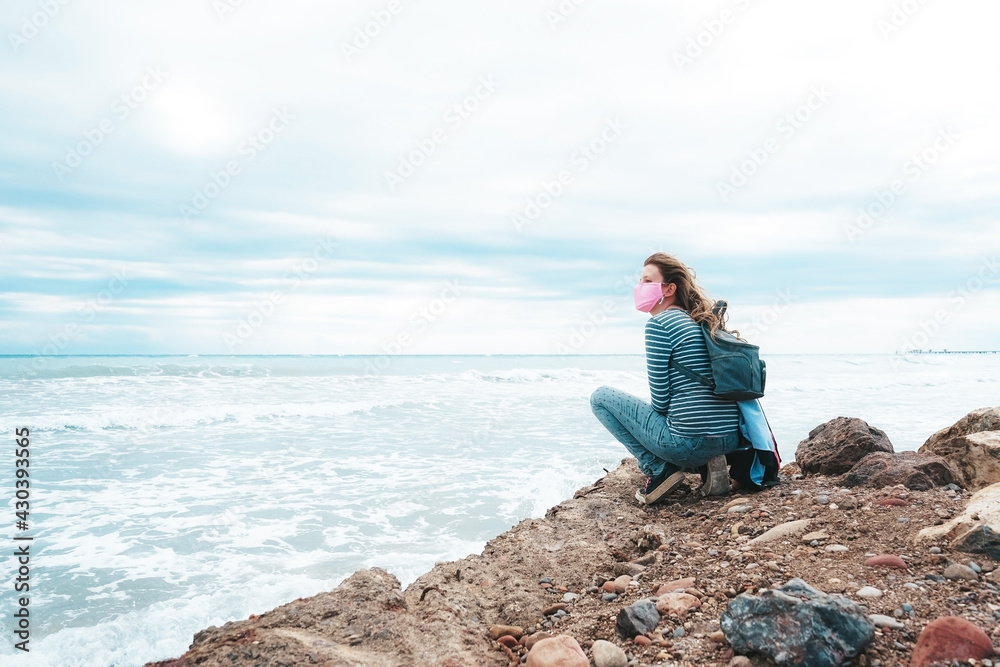 Young woman wearing a pink face mask sitting near the sea