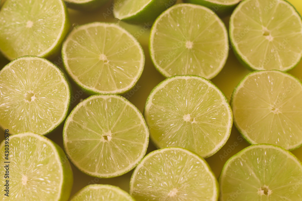 Fresh green juicy limes cut half on yellow background.