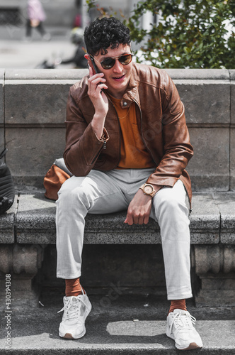 Happy young handsome man wearing spring clothes sitting outdoor in park talking and texting on cellphone © Tato_Torrejon