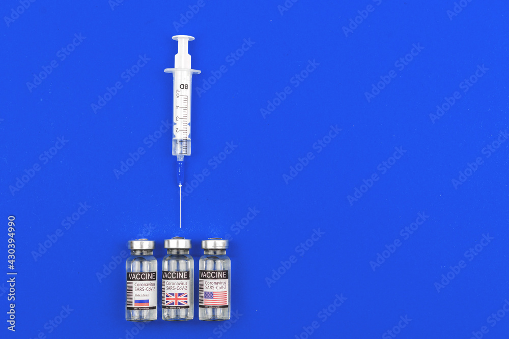 Choosing the best vaccine for vaccination against coronavirus, COVID-19 pandemic, vaccine vials with Russia, USA and UK country flags on the labels, blue background with copy space