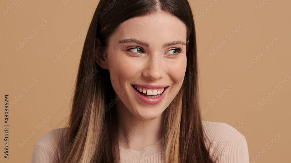 A close-up view of a surprised glad young woman is looking to the camera standing isolated over a beige background in the studio A close-up view of a surprised glad young woman is looking to the camera standing isolated over a beige background in the studio